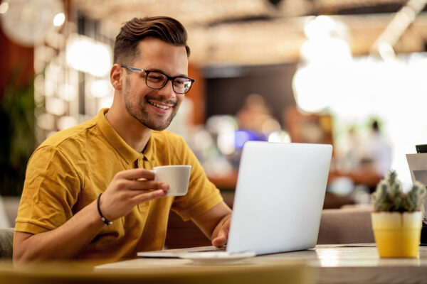 Young happy man using laptop and drinking coffee in a cafe.